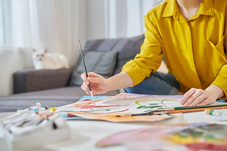 mulher fazendo pinturas em um papel, com pincel e uma folha branca