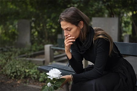 uma mulher, em luto, em um cemitério, de preto, segurando flores para depositar