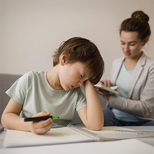 Criança esfregando o rosto com a mão enquanto realiza uma tarefa escolar