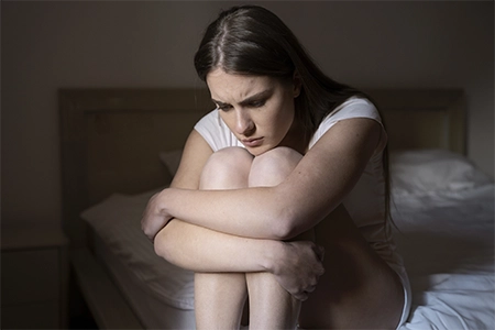 mulher agarrada aos joelhos, sentada na cama, com sinal de tristeza