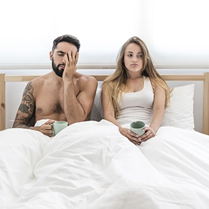 jovem casal sentado na cama com cara de frustração